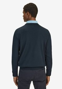 Marinblå stickad tröja med rund halsringning och långa ärmar, med ribbade muddar och fåll. Bärs över en ljusblå skjorta med krage.