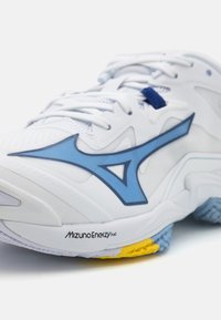 Chaussure de sport blanche avec des accents bleus et une surface texturée. Dotée d'une semelle épaisse avec des détails jaunes et bleus, étiquetée "MizunoEnergy."