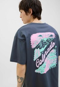 Kortærmet, mørkegrå t-shirt med et stort pink og teal grafik på ryggen, der viser bjerge og ordet "Colorado."