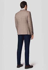 Brązowa marynarka w kratę o dopasowanym kroju, granatowe spodnie i brązowe skórzane buty. Marynarka ma klapę w kształcie notcha i podwójny rozcięcie z tyłu.