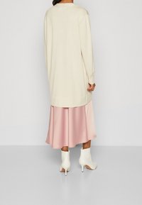 Lång krämfärgad tröja över en blek rosa satin kjol, tillsammans med vita ankelskor. Tyget ser slätt ut med en avslappnad passform och långa ärmar.