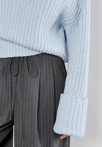 Maglione lavorato a maglia azzurro chiaro con trama a coste, maniche ampie e design corto, abbinato a pantaloni grigi a righe con pieghe.