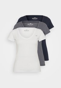 Tres camisetas en blanco y azul marino; una completamente blanca, una azul marino con rayas blancas y una completamente azul marino. Todas tienen un diseño de cuello en V y mangas cortas.