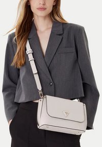 Borsa a mano beige chiaro strutturata con chiusura a patta, dotata di accessori in argento e logo triangolare. Tracolla regolabile, texture liscia.