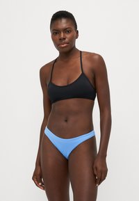 Črni bikini zgornji del s tankimi naramnicami, v kombinaciji s svetlo modrim bikini spodnjim delom z visokim izrezom. Material se zdi gladek z minimalnimi šivi.