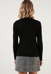 Maglione lungo a maniche lunghe nero con scollatura alta, abbinato a una gonna grigia texturizzata, che mette in risalto una silhouette aderente.