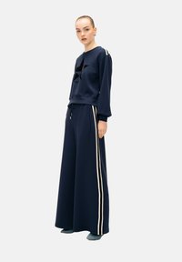 Sweat-shirt bleu marine avec un design d'étoiles noires et des rayures blanches sur les manches, associé à un pantalon large bleu marine avec des rayures blanches sur les côtés.