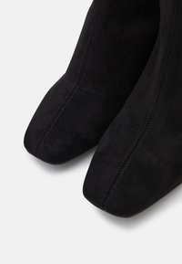 Stivaletti alla caviglia in suede nero con punta affusolata. Presentano cuciture visibili e una texture liscia, che mettono in mostra un design minimalista.