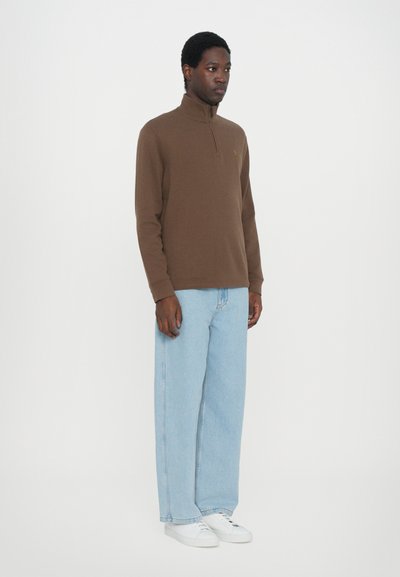 Bruine sweater met rits en een zachte stof, gecombineerd met lichtblauwe wijde jeans en witte sneakers. Eenvoudig, strak ontwerp met minimale accenten.
