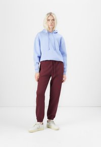 Lyseblå hettegenser med snøring, kombinert med burgunder joggebukser. Joggesko med hvit base og lyse detaljer. Enkel design.