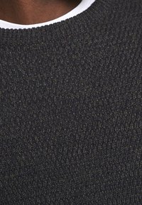 Ciemny sweter z grubym splotem, z prążkowanym, okrągłym dekoltem. Kolor to mieszanka ciemnych odcieni, głównie czerni i oliwkowego.