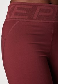 Colanți de sport vișinii cu un tiv înalt texturat și un material neted și elegant pe picioare. Prezintă cusături plate pentru confort și volum minim.