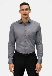 Camicia grigia a maniche lunghe con bottoni, dotata di taschino sul petto, realizzata in tessuto liscio. Caratterizzata da un colletto a punta e dettagli con polsini abbottonati.