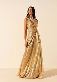 Robe de soirée en or, métallique, avec un tissu drapé, un corsage ajusté et un détail de taille nouée. Longue jusqu'au sol, avec un éclat subtil et une texture lisse.