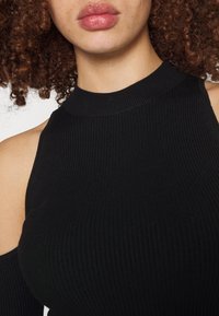 Haut sans manches noir à côtes avec un col montant et des découpes aux épaules, présentant une coupe ajustée et une texture lisse.