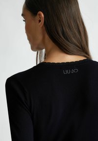 Zwarte trui met een golvende halslijn en een decoratief "LIU JO" logo van strass aan de achterkant. Glad, aansluitend breisel.