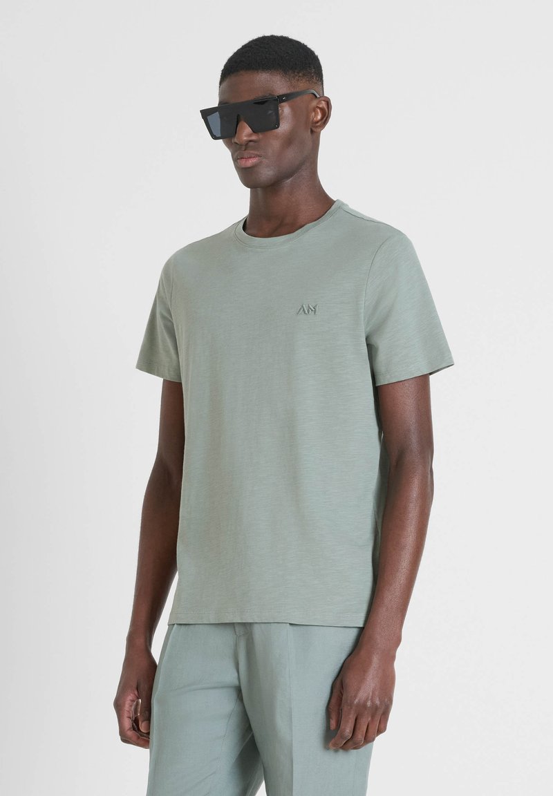 T-shirt verde chiaro a maniche corte con collo rotondo, caratterizzato da un logo ricamato discreto sul petto. Tessuto morbido, vestibilità rilassata.