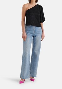 Schwarzes einseitiges Top mit strukturiertem Design, kombiniert mit hellblauen weiten Jeans und pinken spitz zulaufenden High Heels mit Schleifenakzenten.