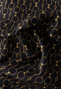 Čierna látka s opakovaným vzorom zlatého reťaze so súvislými kruhovými článkami a mašličkovými ozdobami, vytvárajúca textúrovaný a prepracovaný dizajn.