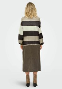 Pull en tricot rayé dans des tons beige, gris et marron ; coupe oversized avec épaules tombantes. Associe à une longue jupe olive et des bottines beiges.
