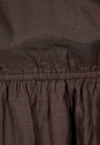 Hnědá tkanina se hladkým povrchem a nařaseným elastickým pasem, s jemnými, subtilními liniemi. Design je volný, vhodný pro každodenní nošení.