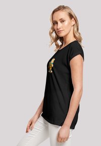 Black short-sleeve t-shirt featuring a cartoon character design on the front. Smooth fabric texture, relaxed fit, paired with white pants.