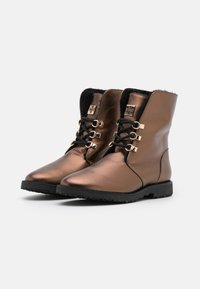 Botas de tobillo metálicas en bronce con forro de ante, cordones frontales con herrajes en tono dorado y suela de goma negra texturizada.