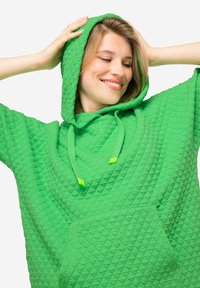 Felpa con cappuccio verde realizzata in tessuto strutturato con un motivo a rombi. Include una tasca frontale e lacci a contrasto.