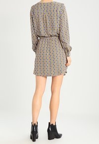 Sukienka z krótkim rękawem w wzorzysty materiał w diamentowe kształty w odcieniach żółtego i brązowego, z talią ściągniętą w pasie oraz krótkim dołem, zestawiona z czarnymi botkami za kostkę.