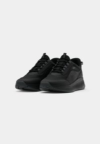 Chaussures de sport noires avec un dessus en tissu texturé, des détails perforés et une semelle en caoutchouc contrastante. Présentent des accents bleus sur les lacets.