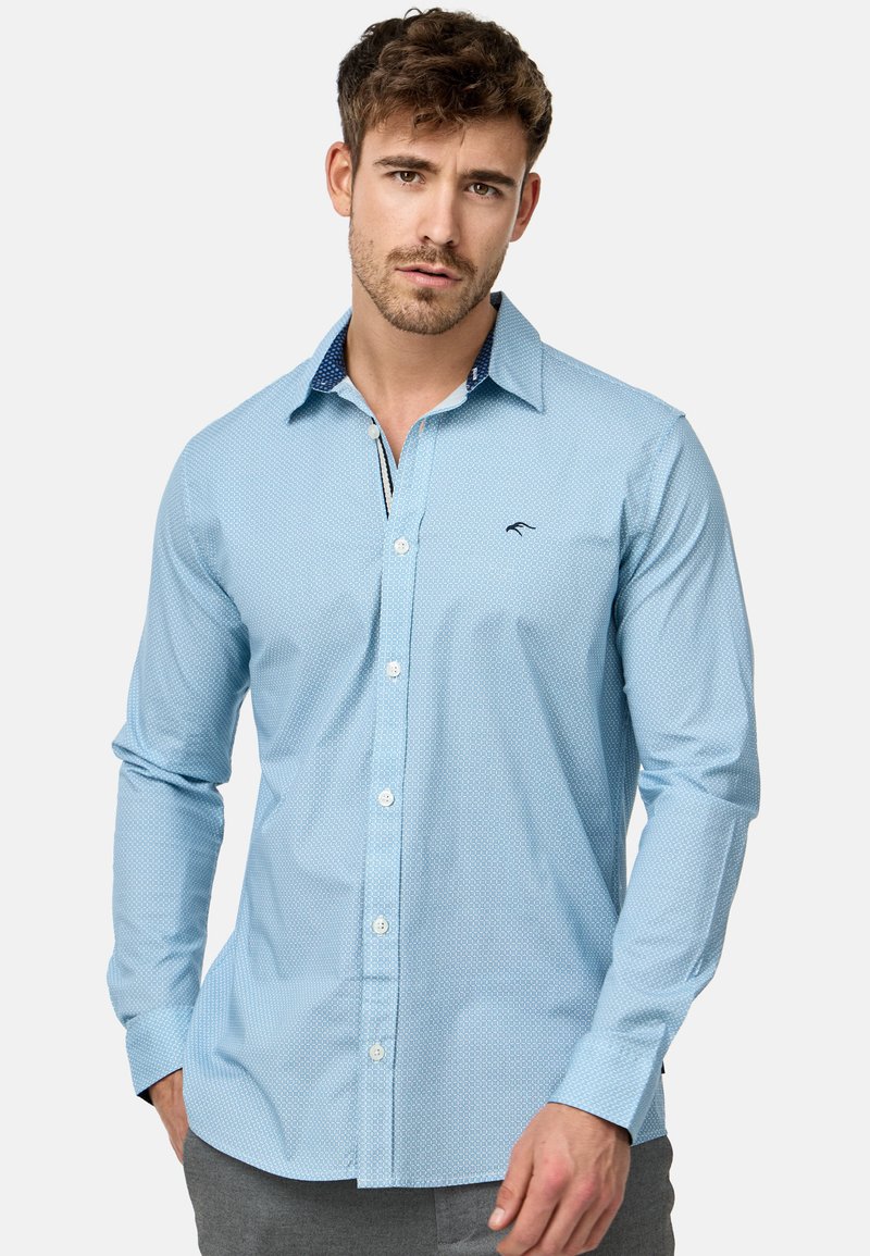Chemise boutonnée bleu clair avec un motif de pois texturé. Dotée d'un col contrastant bleu marine et d'un logo brodé sur la poitrine.