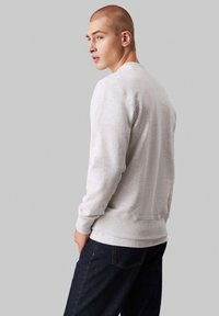 Sudadera gris con cuello redondo, puños y dobladillo acanalados, hecha de una tela suave. Combinada con jeans azul oscuro, mostrada de perfil.