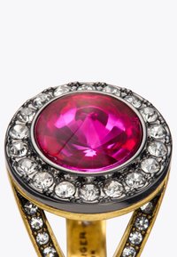 Złoty pierścionek z dużym okrągłym fioletowym kamieniem szlachetnym na środku, otoczony przez przezroczyste cyrkonie, z misternym wzornictwem i detalami.