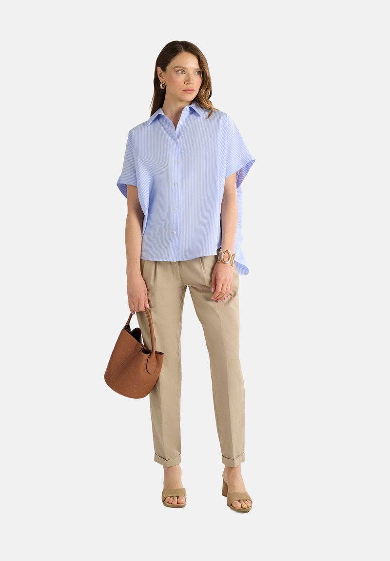 Camicia a righe azzurro chiaro a maniche corte con chiusura a bottoni, abbinata a pantaloni beige attillati e una borsa a secchiello marrone. Sandali con tacco beige.