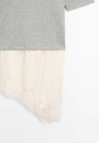 Szary krótki rękaw warstwowany na jasnokremową tkaninę z koronkowym wykończeniem u dołu, tworząc efekt podwójnej warstwy ubrania.