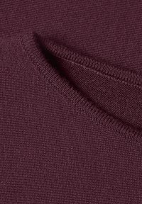 Gros plan d'un tissu tricoté plié violet foncé montrant une texture douce et des détails de couture fins.