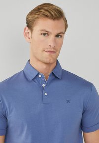 Polo a maniche corte da uomo in blu chiaro, con colletto, apertura con tre bottoni e logo discreto sul petto.