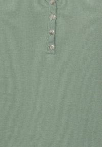 Chemise henley côtelée verte claire avec un devant à boutons comportant cinq boutons en argent brillant et un tissu doux et texturé.