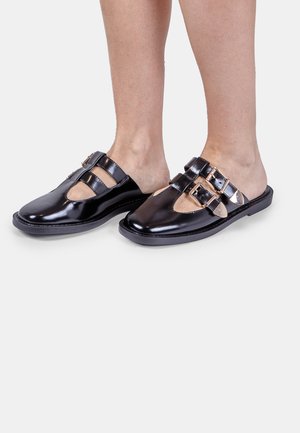 Black patent leather slip-on shoes with a squared toe, featuring open sides and two gold-tone buckle accents. Flat sole.