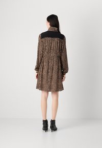 Leopardenmuster-Kleid mit schwarzem Kragen, elastischem Bund und langen Ärmeln. Trägt man mit schwarzen Ankle-Boots, bietet es einen lässigen Schnitt und eine Länge bis über die Knie.