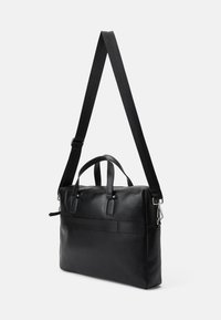 Crna kožna torba s dvostrukim gornjim ručkama i odvojivim podesivim remenom. Ima teksturiranu površinu i jednostavan, moderan dizajn.