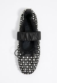 Zapato de cuero negro con tachuelas plateadas, banda elástica parcial y detalle de cordones atados. Punta redondeada y acabado texturizado.