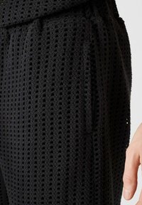 Pantalones de malla negros con un tejido texturizado y rayas verticales, bolsillos laterales y un ajuste cómodo y holgado en la cintura.