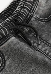 Schwarzgraue, texturierte Jogginghosen mit einem elastischen Bund, der eine Kordel und subtile Verblassungsdetails im Stoff aufweist.