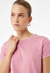 Top de manga corta rosa claro con cuello redondo, que presenta un delicado borde blanco en el escote y las mangas, fabricado con una tela suave y lisa.