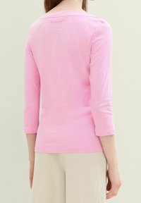 Pink, long-sleeve top with a round neckline and three-quarter sleeves. Made from lightweight fabric, featuring a subtle logo at the back.
