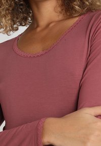 Långärmad topp i dämpad rosenfärg med en vågig halsringning och manschetter, gjord av mjuk tyg, med en slät yta och figurnära design.