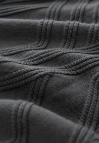 Sötét szürke kötött anyag, kiemelkedő átlós csíkokkal és texturált hullámformákkal, amely hangsúlyozza a puha textúrát és a bonyolult varrást.