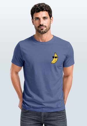Man with dark curly hair wearing a blue t-shirt with a small yellow banana wearing sunglasses graphic on the chest.