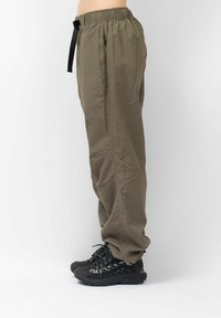 Leichte, olivgrüne Hose mit einem elastischen Bund, schwarzem Kordelzug und Seitentaschen; kombiniert mit robusten schwarzen Schuhen.